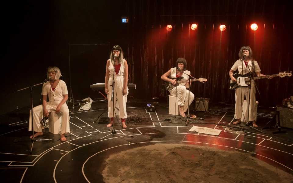 vier Personen stehen mit Musikinstrumenten auf einer Bühne. 